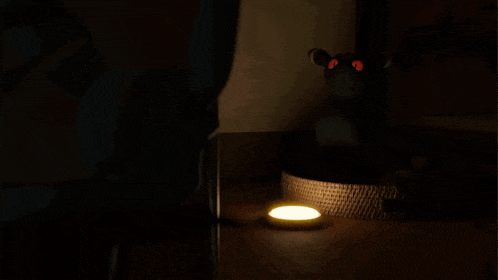 a stuffed animal with red eyes sits in a dark room next to a light