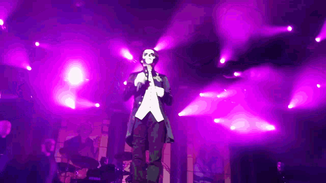 a man in a tuxedo is singing into a microphone in front of purple lights .