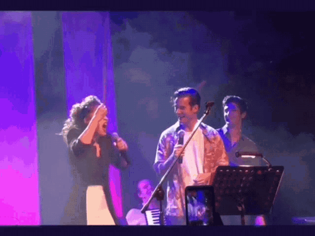 a man and woman singing on a stage with purple lights
