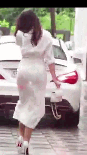 a woman in a white dress and high heels is standing next to a white car .