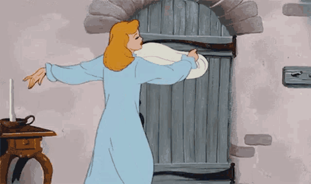 cinderella is wearing a blue nightgown and dancing in front of a door in a cartoon .