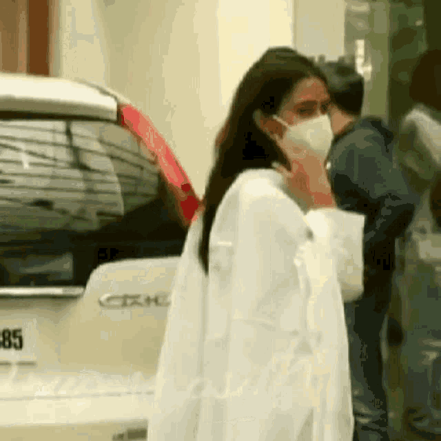 a woman wearing a face mask is standing next to a car .