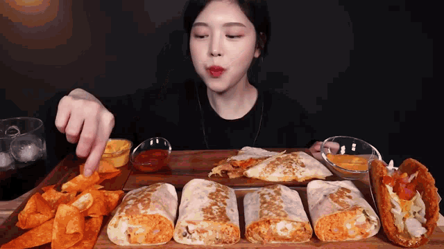 a woman is sitting at a table eating a variety of tacos