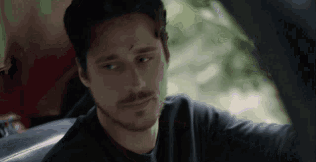 a man with a beard is sitting in a car and looking out the window