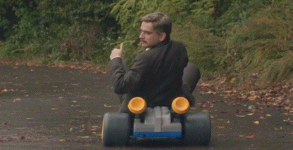 a man with a mustache is riding a go kart on a road .