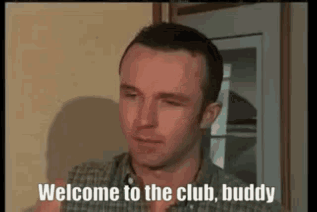 a man in a plaid shirt is talking to another man and says `` welcome to the club buddy '' .