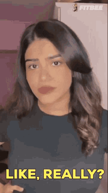 a woman says " like really " in front of a pink wall