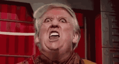 a close up of a man making a funny face with his mouth open in front of a red curtain .