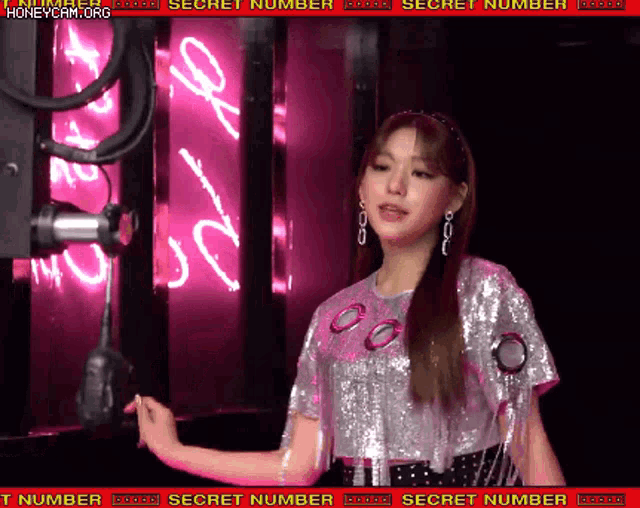 a woman is standing in front of a pink neon sign that says secret number