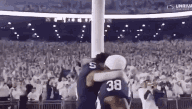 two football players are hugging each other in front of a crowd of people at a stadium .