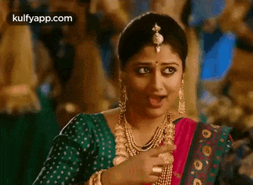 a woman in a green blouse and a pink sari is pointing at her chest .