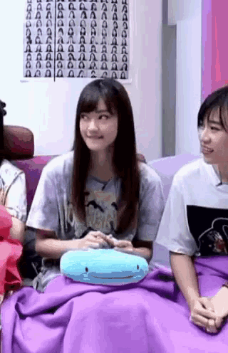 a group of girls are sitting on a couch with a purple blanket .