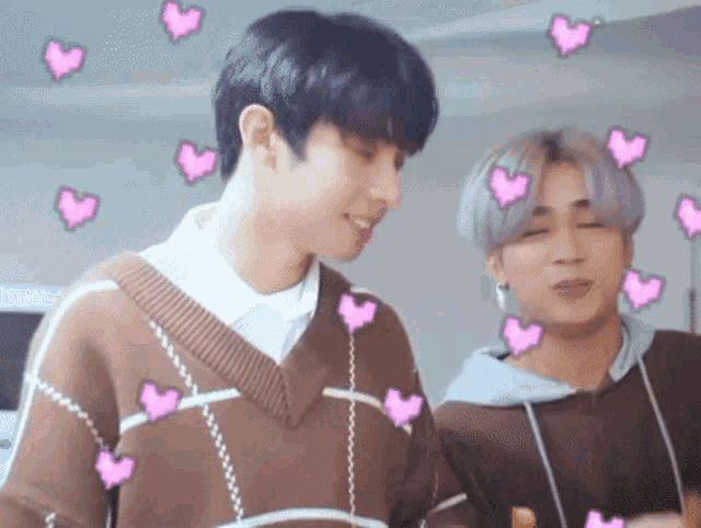 two young men are standing next to each other in a room with hearts around them .