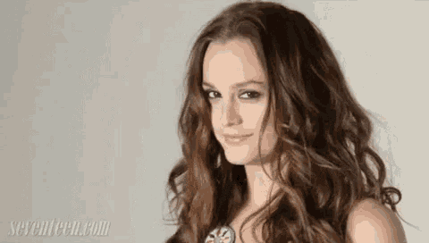 a woman with long curly hair is smiling for the camera .