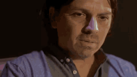 a man with a purple nose is sitting in a dark room .