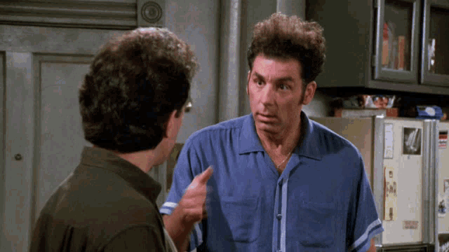 a man in a blue shirt is pointing at another man in front of a fridge