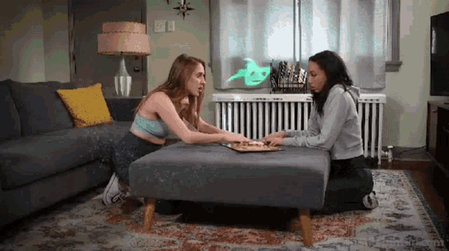 two women are playing a game of ouija in a living room .