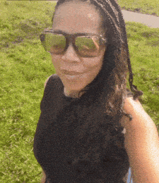 a woman wearing sunglasses and a black shirt is standing in the grass