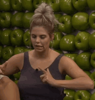 a woman is standing in front of a wall of green apples and making a funny face .