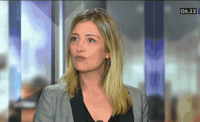 a woman in a grey jacket is on a television screen with the time 06.22