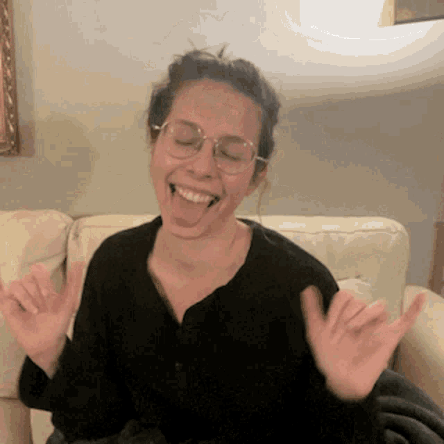 a woman wearing glasses and a black shirt is sitting on a couch and making a funny face