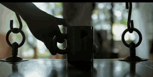 a person 's hand is reaching for a cup of coffee on a table