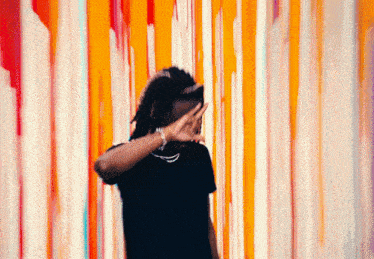a person covering their face with their hand in front of a colorful wall