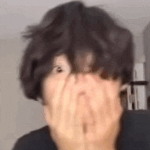 a close up of a person covering their face with their hand .