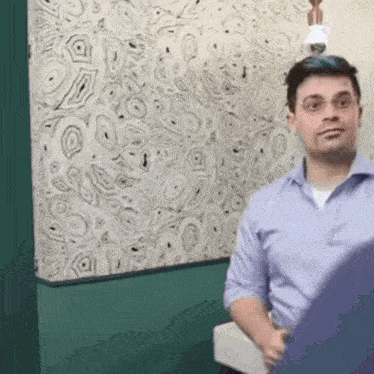 a man in a blue shirt is standing in front of a wall with a pattern