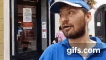 a man wearing a blue hat and a blue shirt is standing in front of a vending machine .