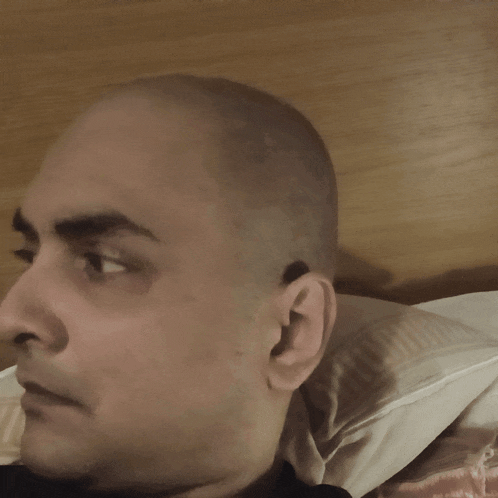 a man with a bald head is laying on a bed with a pillow