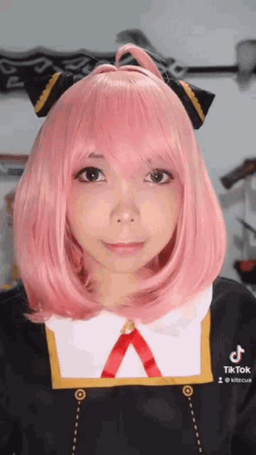 a girl wearing a pink wig and a black and gold outfit has a tiktok account