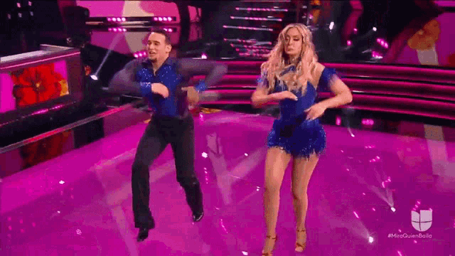 a man and a woman are dancing on a stage with a purple background