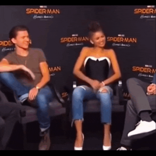 a man and a woman are sitting next to each other on a couch in front of a spider man sign .