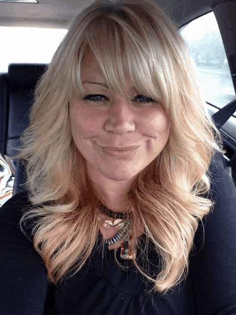 a woman with blonde hair is smiling and wearing a necklace