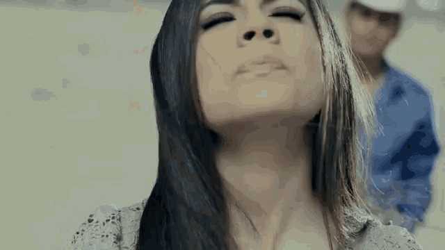 a woman with long hair is making a funny face with her eyes closed and a man in the background .