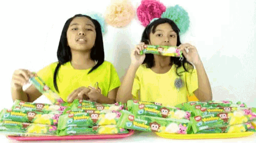 two girls in yellow shirts are eating candy that says monkey on it