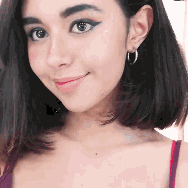 a woman wearing hoop earrings and a purple tank top smiles for the camera