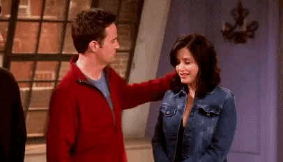 a man in a red jacket is petting a woman in a denim jacket on a television show .