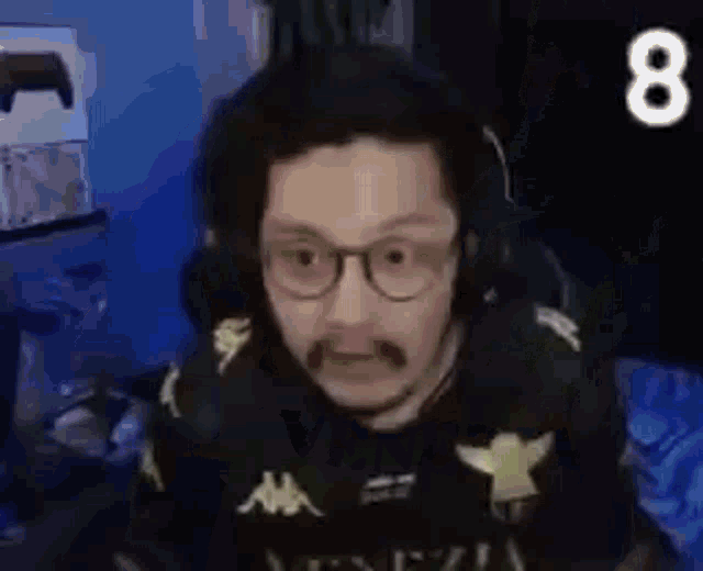 a man with glasses and a mustache is wearing headphones while sitting in front of a computer .