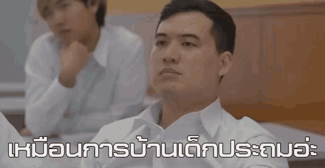 a man in a white shirt is sitting next to another man in a classroom with a foreign language written on the bottom