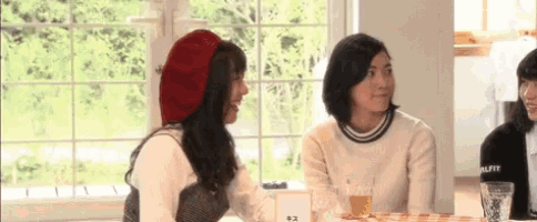 two women are sitting at a table talking to each other . one is wearing a red beret .