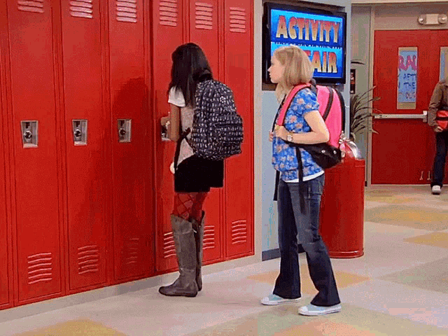 two girls are standing in front of red lockers in a hallway with a sign that says activity fair on it