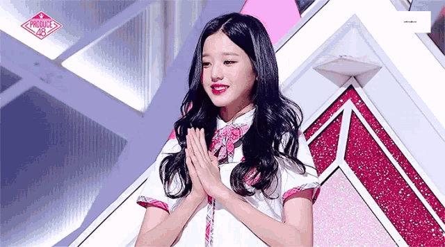 a young woman with long black hair is standing on a stage with her hands folded in front of her face .