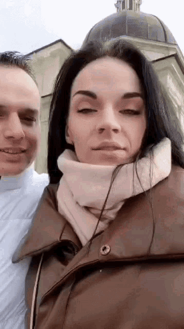 a man and a woman are posing for a picture in front of a building .