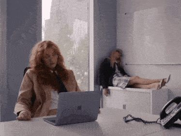 a woman sitting at a desk with an apple laptop and a phone that says ' telephone ' on it