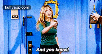 a woman in a green shirt is standing in front of a blue door and saying and you know .