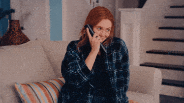 a woman in a plaid shirt is sitting on a couch talking on a cell phone