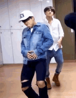 a man in a denim jacket is standing next to another man in a white shirt and hat .