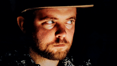 a man with a beard is wearing a hat and looking at the camera